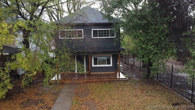 view of front facade featuring roof with shingles, fence, and covered porch