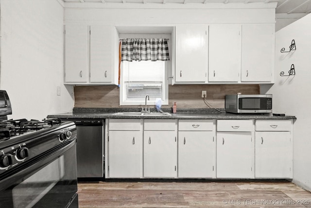 kitchen with stainless steel appliances, dark countertops, white cabinetry, and a sink