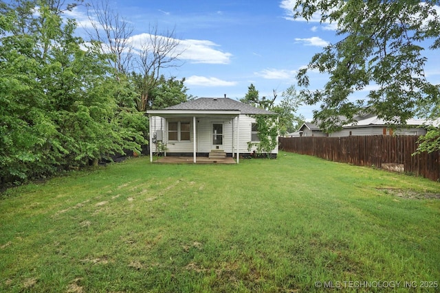 rear view of property with roof with shingles, fence, and a yard