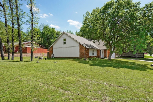 exterior space with brick siding, a shingled roof, fence, and a yard