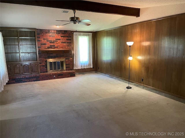 unfurnished living room featuring wooden walls, ceiling fan, a fireplace, beamed ceiling, and visible vents
