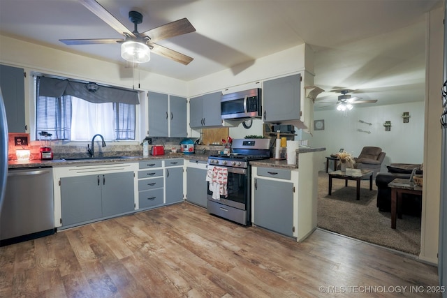 kitchen with appliances with stainless steel finishes, a sink, light wood-style floors, a ceiling fan, and decorative backsplash
