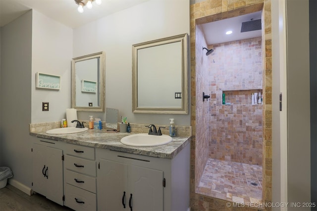 full bathroom featuring double vanity, tiled shower, a sink, and visible vents