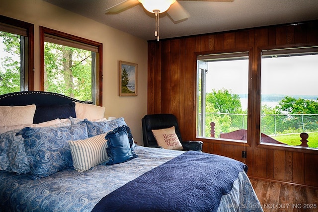 bedroom with wooden walls, a ceiling fan, and wood finished floors