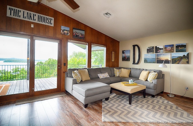 living area with wooden walls, visible vents, a ceiling fan, wood finished floors, and vaulted ceiling