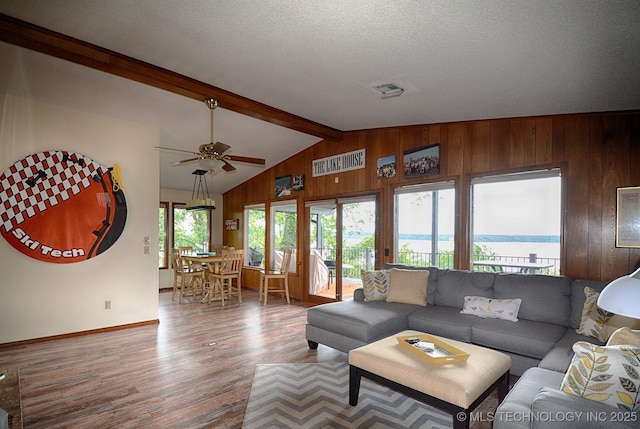 living area with wood walls, wood finished floors, baseboards, ceiling fan, and vaulted ceiling with beams