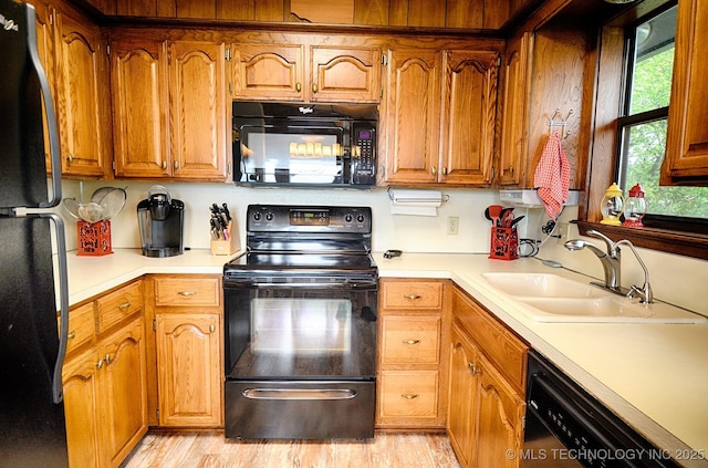 kitchen featuring brown cabinetry, a sink, black appliances, and light countertops