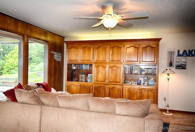 living area with a ceiling fan, a textured ceiling, wood finished floors, and wooden walls
