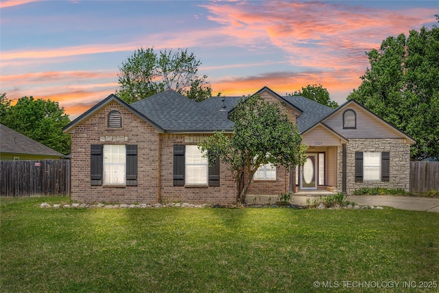 view of front of house with fence, a shingled roof, a front lawn, and brick siding