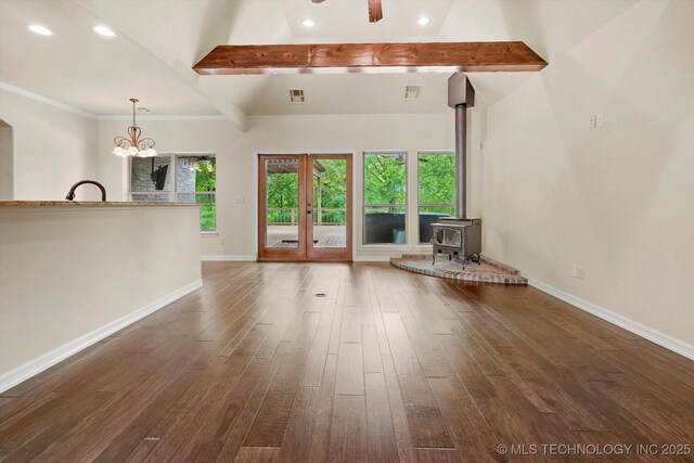unfurnished living room with visible vents, a wood stove, beam ceiling, baseboards, and dark wood-style floors