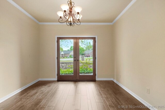 spare room featuring french doors, crown molding, wood finished floors, baseboards, and a chandelier