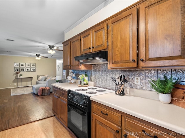 kitchen featuring decorative backsplash, black range with electric cooktop, under cabinet range hood, and brown cabinets