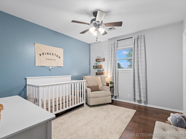 bedroom with visible vents, wood finished floors, baseboards, ceiling fan, and a crib