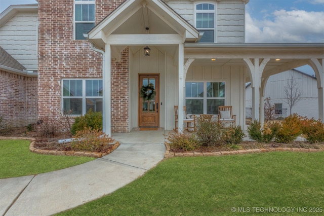 doorway to property featuring brick siding, board and batten siding, a yard, and covered porch