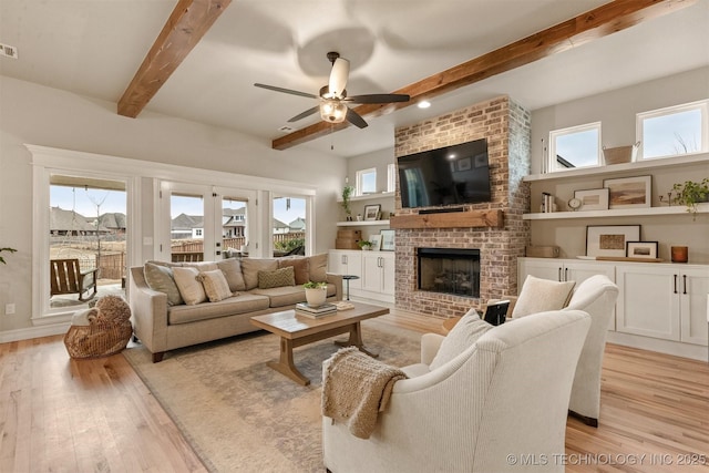 living room featuring beam ceiling, light wood finished floors, a fireplace, a ceiling fan, and baseboards