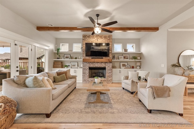 living room featuring a ceiling fan, a fireplace, wood finished floors, and beam ceiling