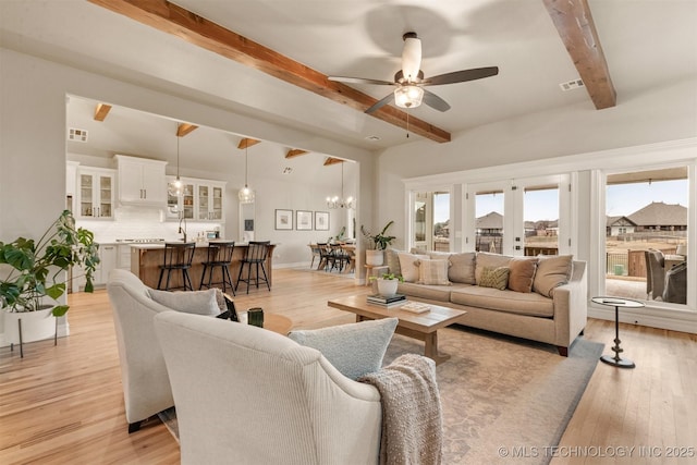living room featuring beam ceiling, ceiling fan with notable chandelier, and light wood-type flooring