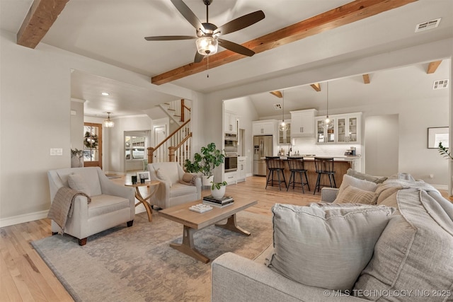 living area featuring visible vents, light wood finished floors, ceiling fan, and beam ceiling
