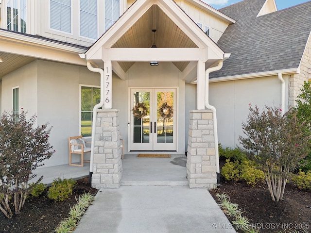 doorway to property with french doors, a shingled roof, stone siding, and stucco siding