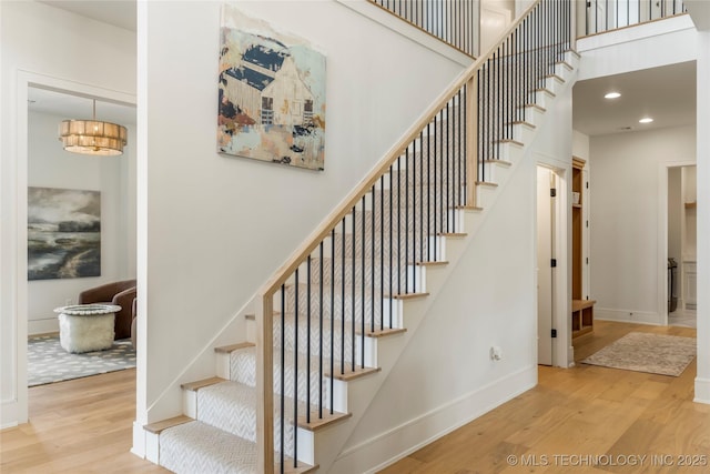 stairway featuring baseboards, recessed lighting, a towering ceiling, and wood finished floors