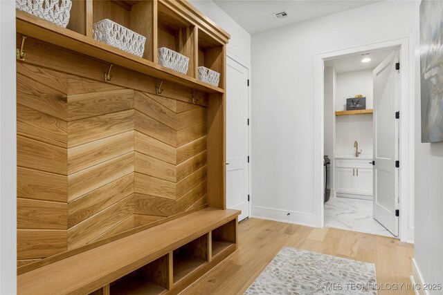 mudroom with baseboards, visible vents, a sink, and light wood-style floors