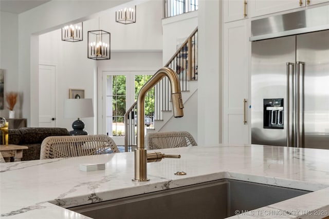 kitchen featuring light stone countertops, a sink, a notable chandelier, stainless steel built in refrigerator, and white cabinetry