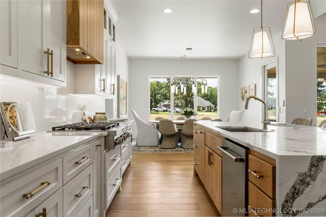 kitchen featuring a kitchen island with sink, decorative light fixtures, appliances with stainless steel finishes, a sink, and light wood-style flooring