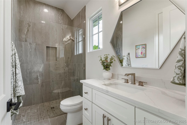 bathroom featuring toilet, a tile shower, tile patterned flooring, and vanity