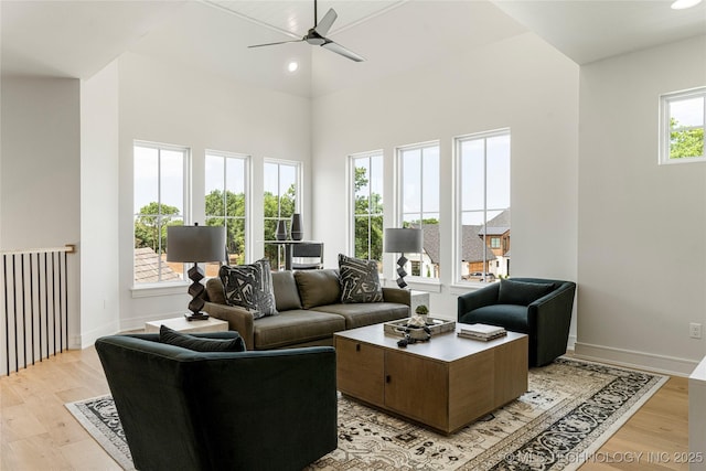 living room with baseboards, a ceiling fan, light wood finished floors, and a towering ceiling