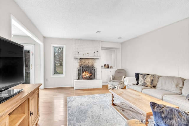2918 S Ash Pl, Broken Arrow, OK 74012 - living room with visible vents, a textured ceiling, light wood-style flooring, and a brick fireplace