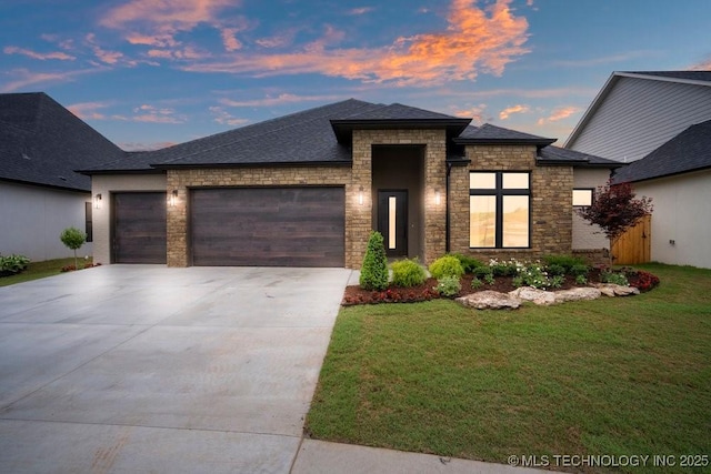 prairie-style house featuring a shingled roof, a garage, a yard, concrete driveway, and stone siding