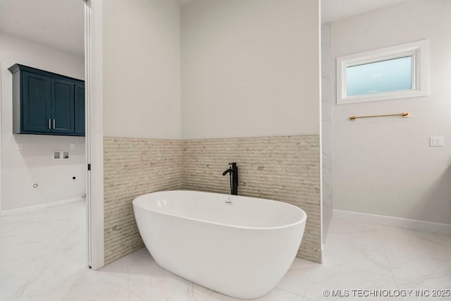 full bathroom with marble finish floor, a freestanding bath, wainscoting, and tile walls