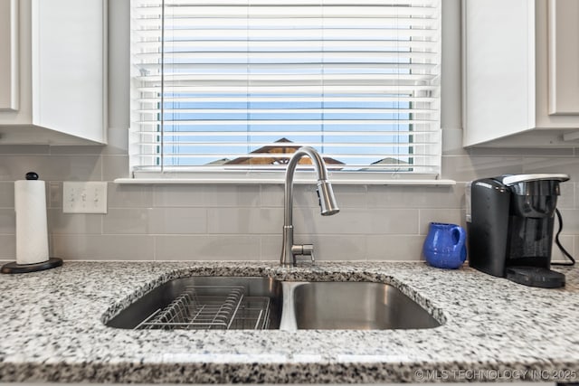 interior details with white cabinetry, light stone countertops, a sink, and tasteful backsplash