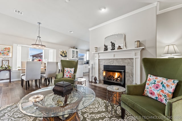 living area featuring wood-type flooring, ornamental molding, visible vents, lofted ceiling, and a fireplace