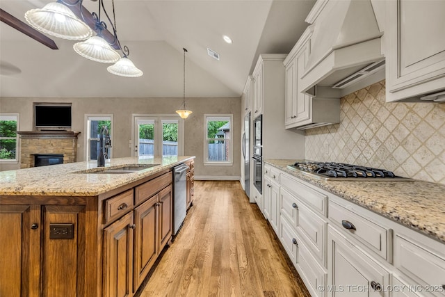 kitchen featuring appliances with stainless steel finishes, light wood-type flooring, brown cabinets, a sink, and custom range hood