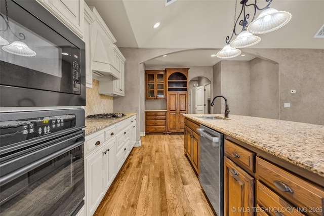 kitchen with light wood-style floors, arched walkways, white cabinets, a sink, and black appliances