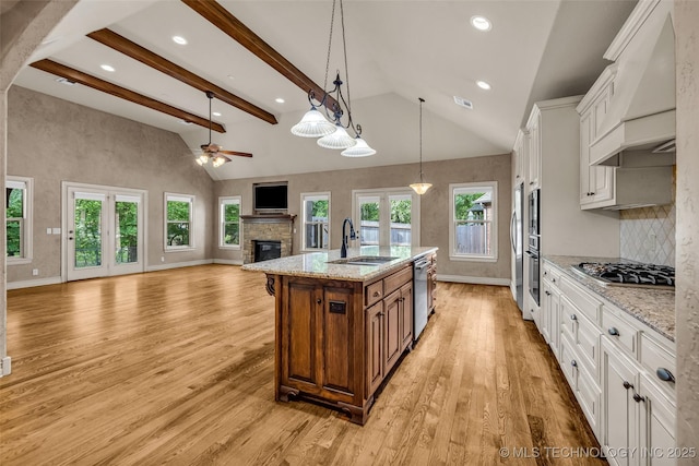 kitchen with a sink, a stone fireplace, premium range hood, baseboards, and open floor plan