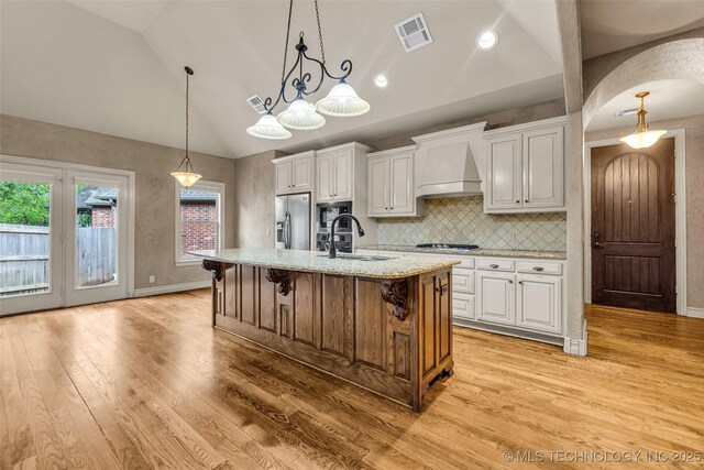 kitchen with visible vents, lofted ceiling, custom exhaust hood, a sink, and appliances with stainless steel finishes