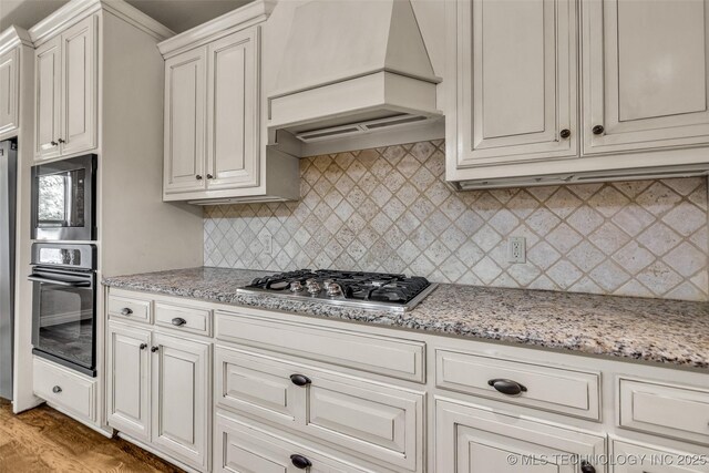kitchen featuring oven, premium range hood, built in microwave, tasteful backsplash, and stainless steel gas stovetop