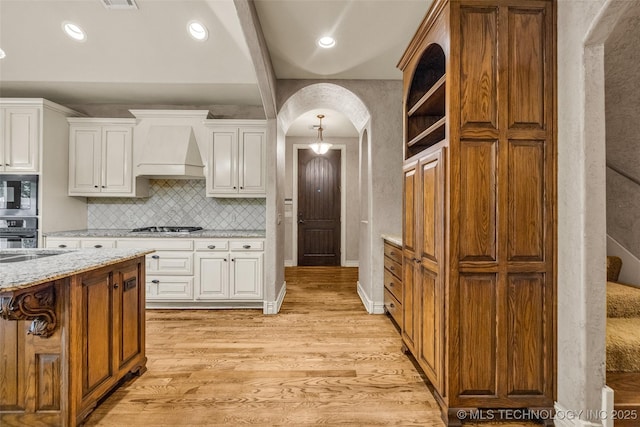 kitchen featuring arched walkways, white cabinetry, light wood-style flooring, and custom range hood
