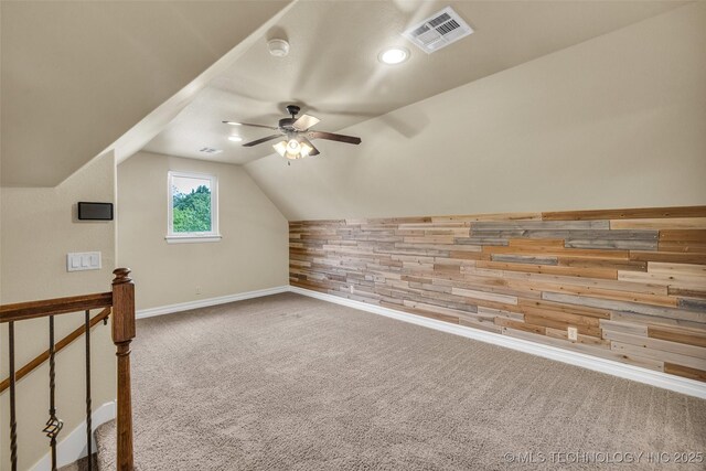 additional living space with a ceiling fan, visible vents, vaulted ceiling, wood walls, and carpet floors