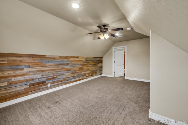 bonus room with lofted ceiling, baseboards, wooden walls, a ceiling fan, and carpet