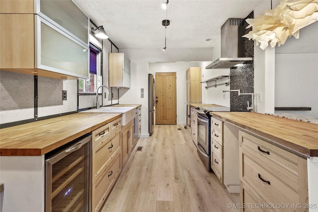 kitchen featuring beverage cooler, wall chimney exhaust hood, a sink, wood counters, and appliances with stainless steel finishes