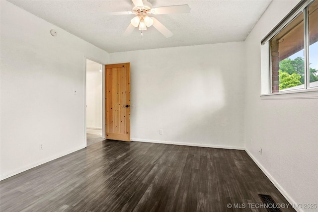 spare room featuring baseboards, a ceiling fan, dark wood-style flooring, and a textured ceiling
