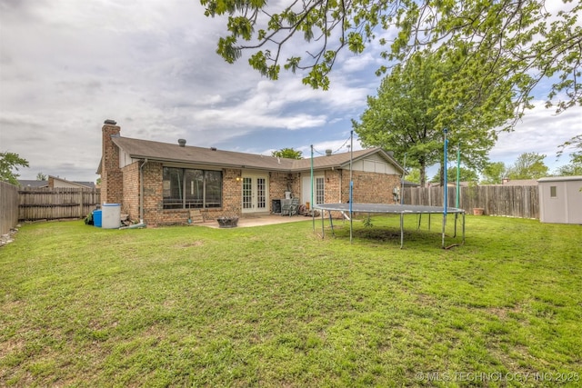back of property with french doors, a chimney, a trampoline, brick siding, and a patio
