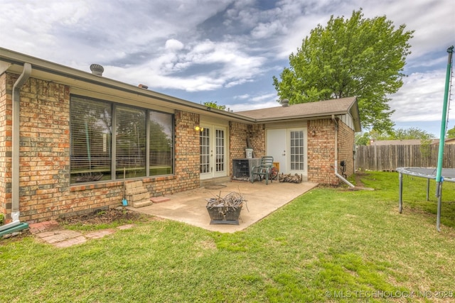 back of property with fence, a trampoline, brick siding, a patio area, and french doors