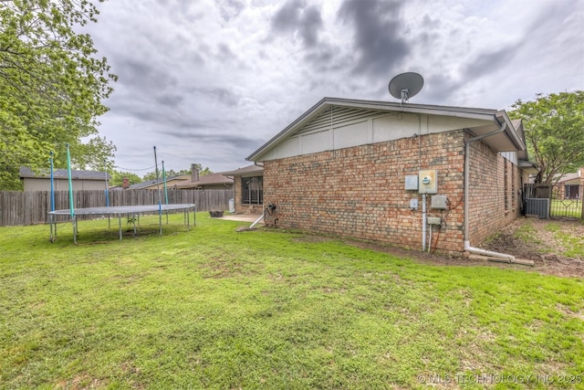 rear view of property featuring a fenced backyard, a trampoline, a yard, and brick siding