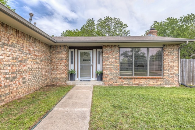 property entrance with brick siding, a lawn, fence, and a chimney