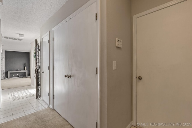 hallway with light tile patterned floors, light colored carpet, a textured ceiling, and visible vents