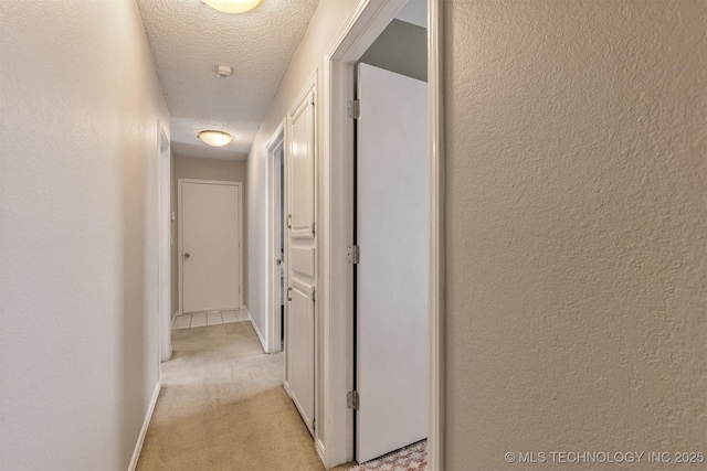 corridor with light colored carpet, a textured ceiling, and baseboards